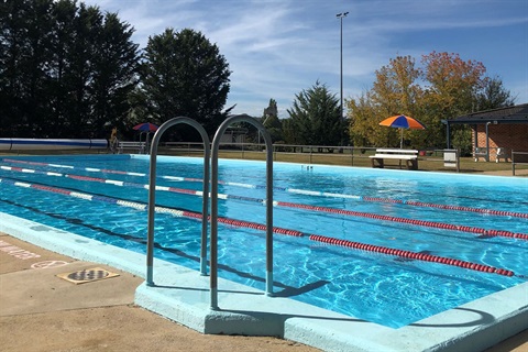 Close-up image of Berridale Pool in summer, with trees, grass and brick building in background