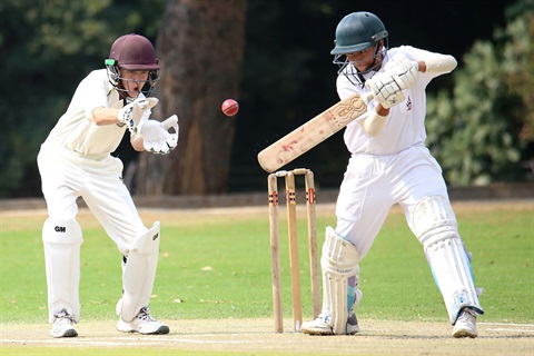 Two children from opposing teams playing cricket, the batter has edged the ball and the wicketkeeper's mouth is open as he goes for the catch.