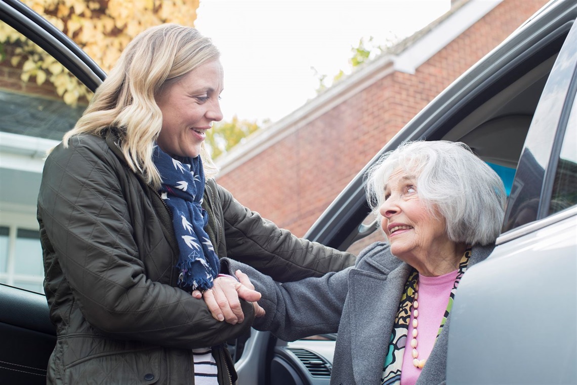 Female volunteer driver providing older woman assistance out of car 