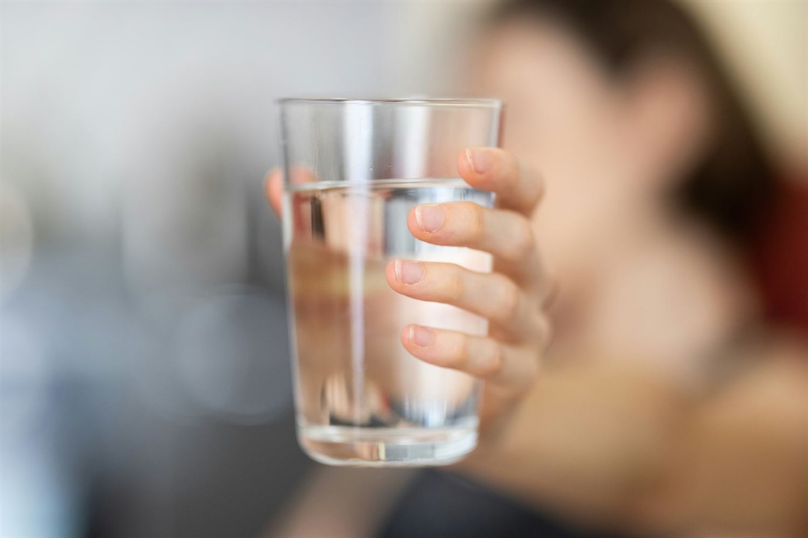 A hand holding a clear glass of water up to the camera