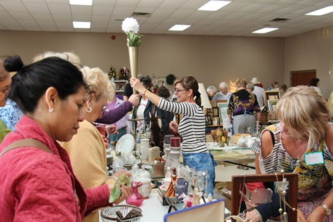 Patrons browse and barter the trestle tables of secondhand goodies at an indoor garage sale.