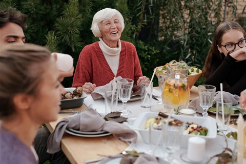 Multiple generations of a family seated around an outdoor dining table for a meal, laughing and smiling