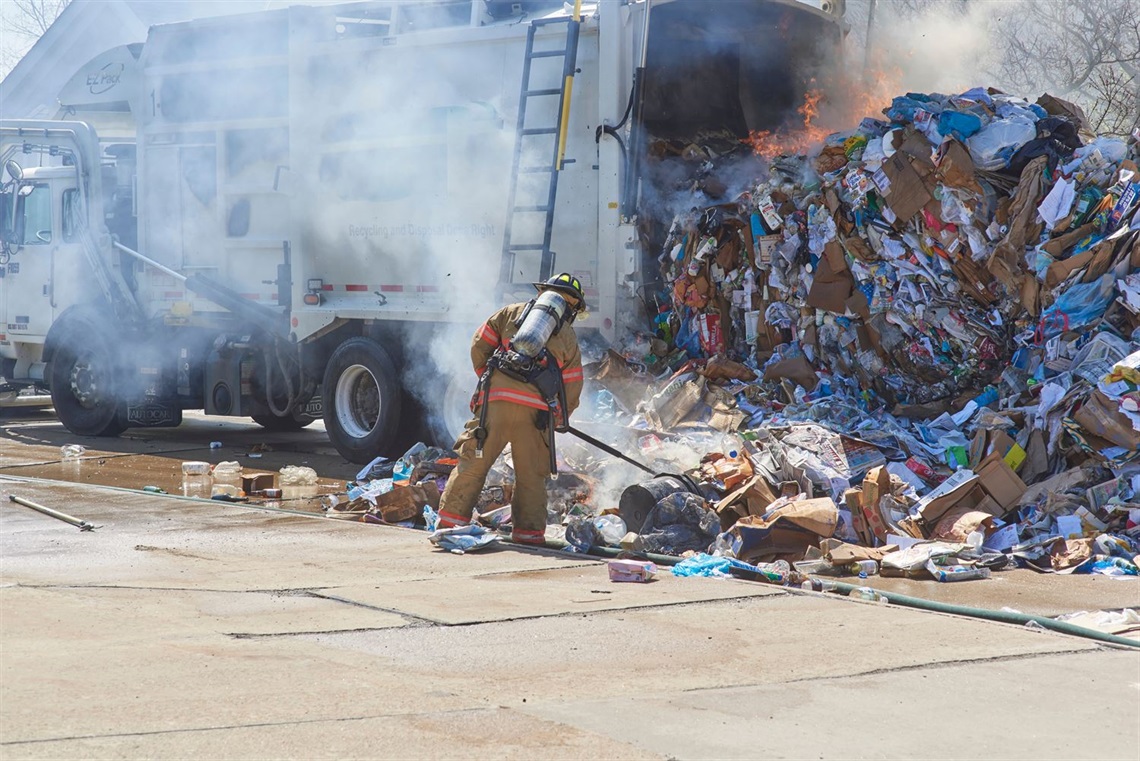 A firefighter extinguishing the last of a fire in the waste hold of a rubbish truck.