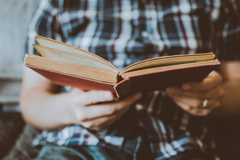 A close-up photo of an old book open in a male reader's hands.