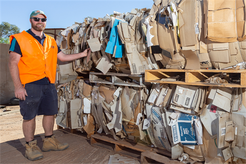 A man in high vis and sunglasses stands smiling next to a pallet of cardboard recylables.