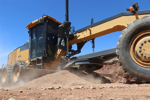 A large yellow grader working on an unsealed (gravel) road