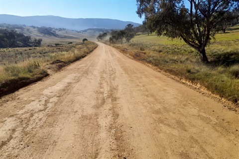 Gravel section of Shannons Flat Road, looking downhill with gumtrees, paddocks and hills in the background. 