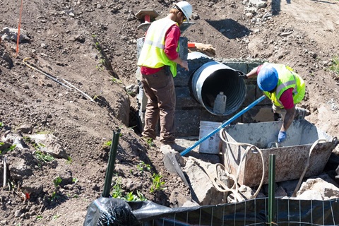 Construction workers building a retaining wall around a newly-installed under-road culvert.
