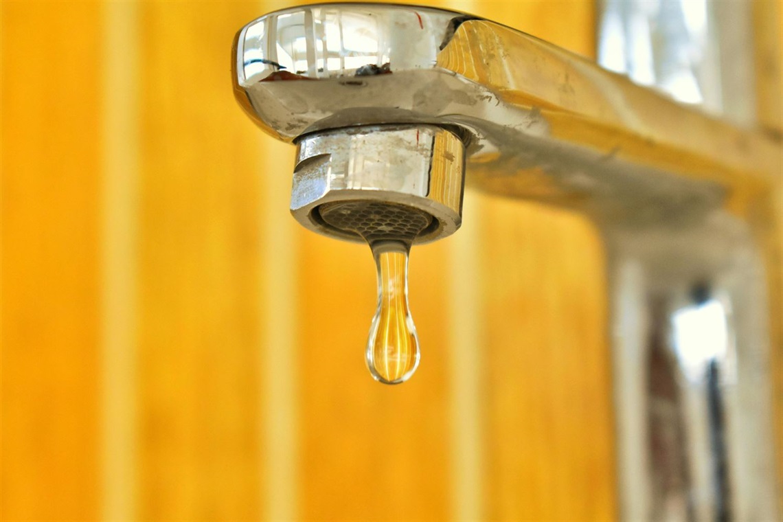 Tap turned off with single drip hanging in front of a yellow splashback