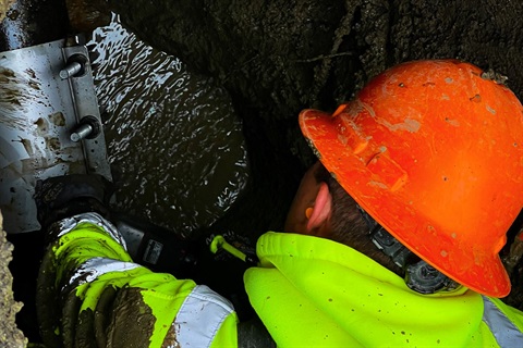 Worker in hard-hat and high vis hooded sweatshirt performing water supply maintenance in an excavated trench